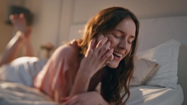 Smiling female speaking mobile phone lying bed in morning sunlight close up. Relaxed beautiful girl talking with partner ending conversation indoors. Gentle peaceful woman resting home hang up call. - Footage, Video