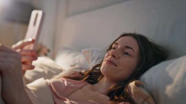 Крупним планом розслаблена дівчина дивиться відео в ліжку. Позитивна жінка, яка проводить конференцію з мобільних телефонів з партнером вранці. Посміхаючись безтурботним жіночим викликам онлайн обговорюйте вихідні. Концепція віртуальної зустрічі - Кадри, відео