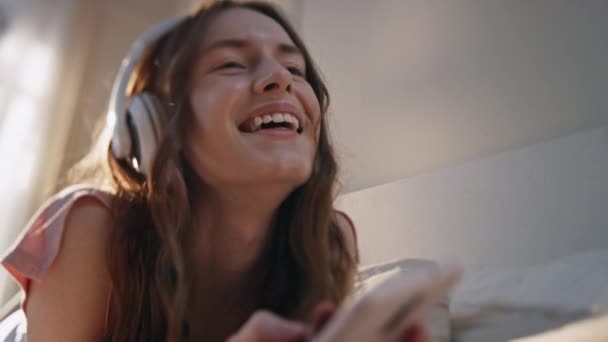 Безтурботна дівчина слухає музику навушників крупним планом. Усміхнена жінка переглядає мобільний телефон, розважається вдома. Радісна красива жінка насолоджується вільним часом, вводячи повідомлення про смартфон. Щасливий спосіб життя підлітків - Кадри, відео