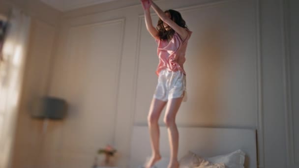 Mulher excitada a saltar para a cama de manhã. Feliz linda menina dança em casa em pijama movendo-se para playlist de música energética. Joyful modelo magro relaxante desfrutando de tempo sozinho. Mulher sorridente celebrando a liberdade - Filmagem, Vídeo
