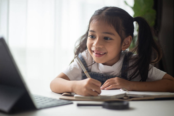 Молода азіатська мила дівчина вчиться з ноутбуком вдома. Концепція онлайн навчання. - Фото, зображення
