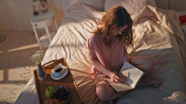自宅で日記を書いている女性. リラックスしたティーンエイジャーは,ノートブックで創造的なアイデアを共有することを夢見ています. 居心地の良い寝室のインテリアでメモを作成する喜びに焦点を当てた女性. 朝のインスピレーションコンセプト. - 映像、動画