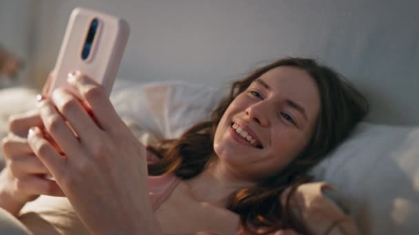 Zorgeloos meisje genieten van virtuele oproep thuis closeup. Glimlachende vrouw die 's morgens in bed ligt te filmen. Gelukkige ontspannen vrouw die online praat en geniet van een positief gesprek. lui tiener spreken vrienden - Video