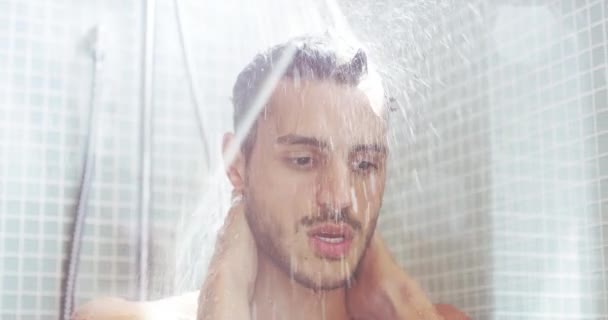 Man, shower and face in cleaning, washing or hygiene for grooming with water splash in bathroom at home. Young, handsome or attractive male person in relax for clean body, care or refreshing at house. - Footage, Video