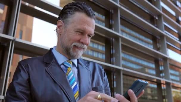 Portret van senior executive sales zakenman zich opgewonden te vieren goed nieuws of zakelijke prestatie na het lezen van onverwachte boodschap op mobiele telefoon buiten. - Video