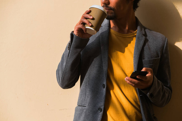 Homem de negócios latino desconhecido bebe café enquanto usa seu telefone inteligente. Espaço de cópia. - Foto, Imagem