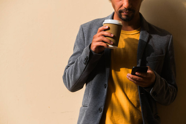 Unknown Latino businessman using his cell phone with a coffee in his hand. Copy space. - Photo, Image