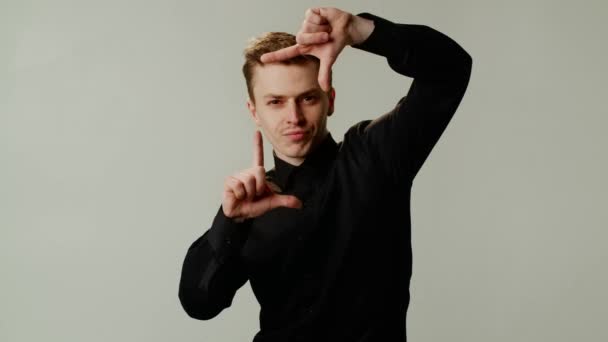 Een stijlvolle man poseert voor een foto- en videoapparatuuradvertentie. Een man film producent of fotograaf gebruikt de wijsvinger en duim van beide handen om een rechthoek te maken en door te kijken - Video