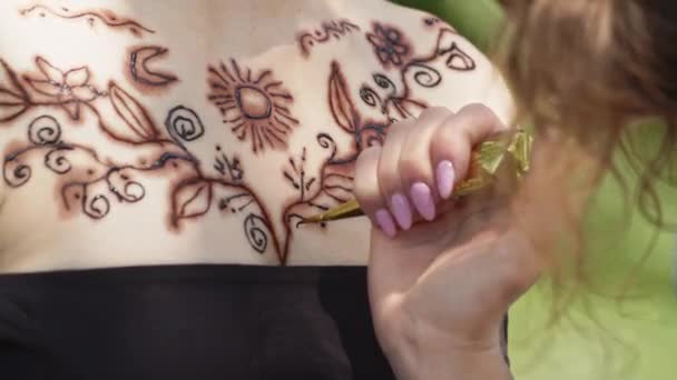 Una giovane ragazza in abito nero fa tatuaggio hennè sul petto con un modello orientale indiano. Una donna tatuatrice professionista applica un disegno con uno strumento speciale. Chiudete. Filmati 4k di alta qualità - Filmati, video