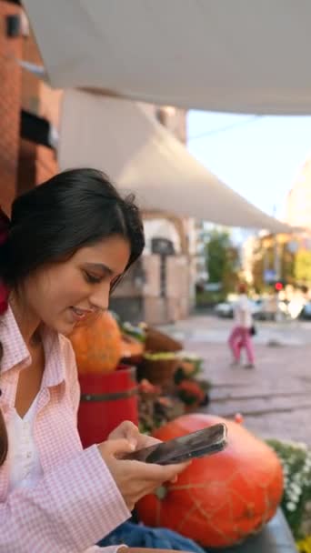 Egy elbűvölő fiatal hölgy, rózsaszínbe öltözve, okostelefonnal, aki a termelői piacot böngészi. Kiváló minőségű 4k felvételek - Felvétel, videó