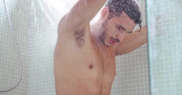 Man, shower and water splash in relax, cleaning or washing for wellness or grooming in bathroom at home. Young, handsome or attractive calm male person in clean body, self care or refreshing at house. - Footage, Video