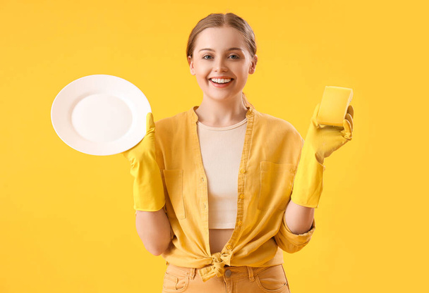 Молодая женщина с тарелкой и губкой на желтом фоне - Фото, изображение