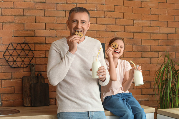 キッチンでミルクを飲むクッキーと小さな少女と彼女の父親 - 写真・画像
