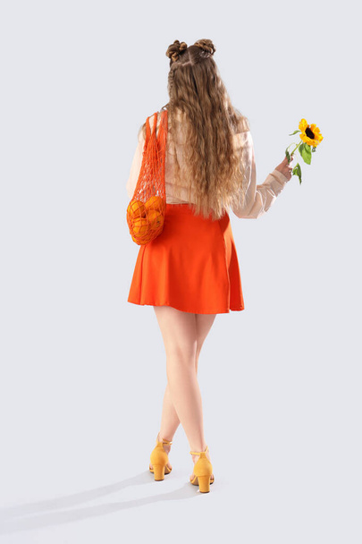 Mujer joven con hermoso girasol y bolsa de hilo sobre fondo claro, vista trasera - Foto, Imagen