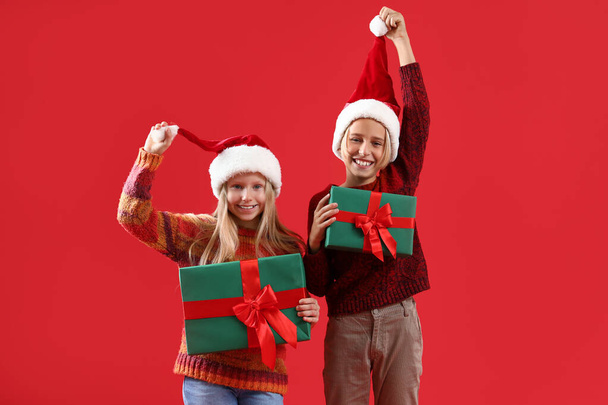 Μικρά παιδιά σε Σάντα καπέλα με χριστουγεννιάτικα δώρα σε κόκκινο φόντο - Φωτογραφία, εικόνα