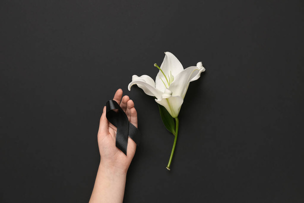 Female hand with ribbon and lily flower on black background - Photo, Image