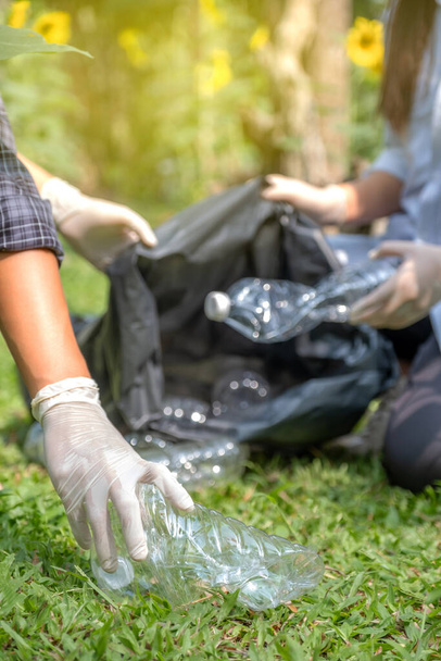 Ręczne trzymanie plastikowych butelek odpadów, para zbierająca śmieci do czarnego worka na śmieci w Sunflower Park w dniu Ziemi Środowiskowej. - Zdjęcie, obraz