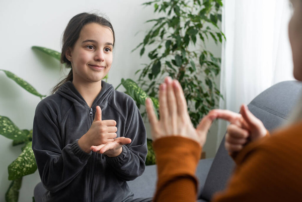 daughter talk with middle aged mother people using sign language, family sitting on armchair side view, teacher teach teenager deaf-mute girl to visual-manual gestures symbols concept image. - Photo, Image