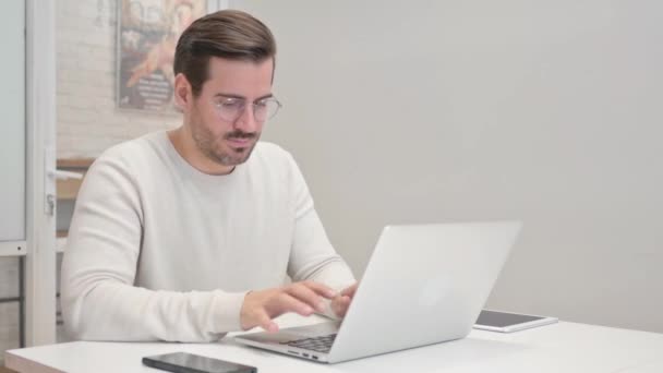 Hombre de mediana edad sonriendo a la cámara mientras trabaja en el ordenador portátil en la oficina - Metraje, vídeo