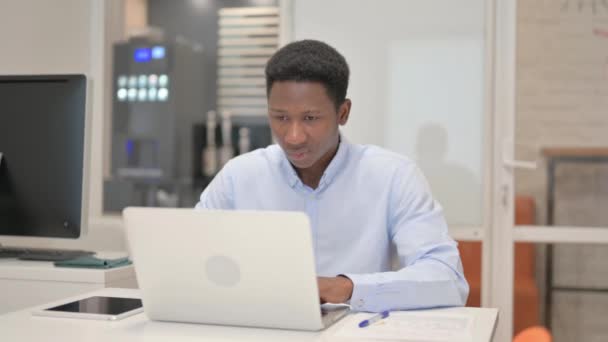 Afrikai üzletember Nézi a kamerát, miközben a Laptopon dolgozik az irodában - Felvétel, videó
