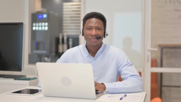 Polegares para cima por homem africano com fone de ouvido usando laptop em Call Center - Filmagem, Vídeo
