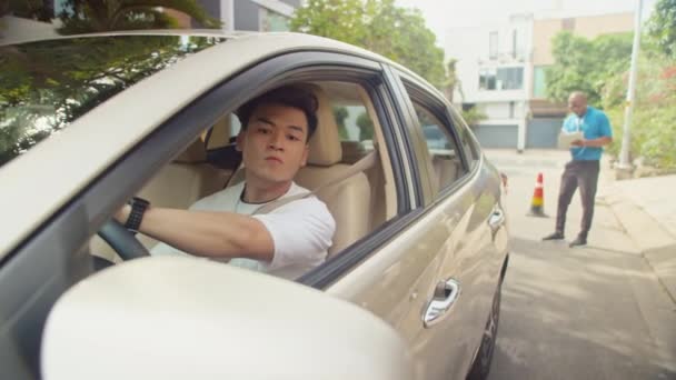 Азіатський чоловік тренує зворотній паркінг між шишками під час здачі іспиту під наглядом інструктора водіння - Кадри, відео