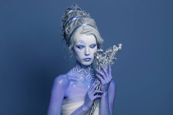 Pretty Snow Queen or Winter Witch woman with perfect fantasy makeup and painted body on blue background. Carnival and Halloween fashion beauty portrait - Photo, image