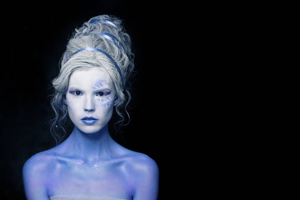 Fantazyjny makijaż. Ładny model kobieta z białą i niebieską skórą i kreatywną fryzurą na czarnym tle - Zdjęcie, obraz