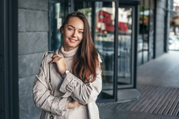 Portrait of a happy young woman against the background of an office building wearing a trench coat. copy space - Photo, Image