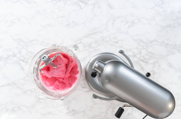 Pose plate. Mélange d'ingrédients dans un mélangeur électrique de cuisine pour faire ombre rose crème au beurre glaçage. - Photo, image