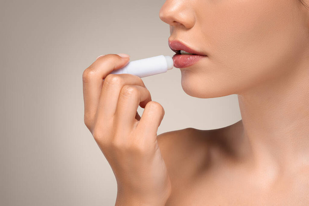 Calm young caucasian woman with perfect skin apply lip balm, enjoy routine procedures, isolated on gray studio background, cropped. Moisturizing, nude makeup, beauty care - Photo, Image