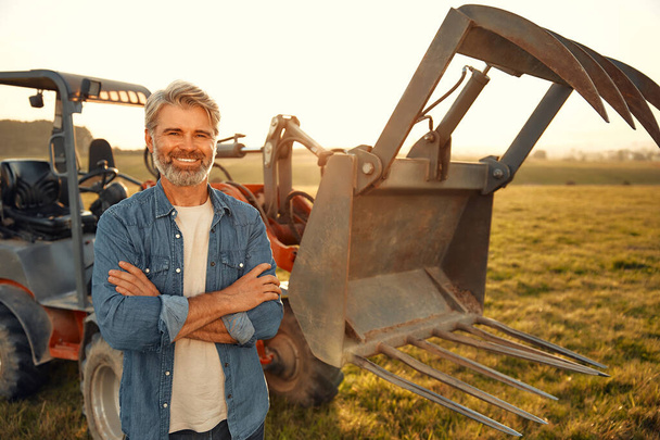 Mature handsome male farmer standing near a tractor on a field on a hot day and working on the farm. Agriculture and agriculture concept. - Photo, Image