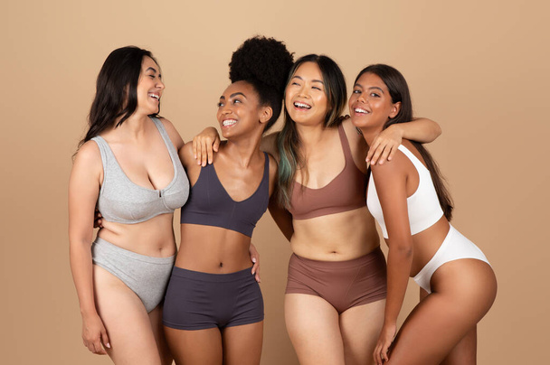 Diverse Frauen präsentieren ihre natürliche Schönheit in dezenter Unterwäsche und teilen einen Moment der Freude und Einheit vor beiger Studiokulisse - Foto, Bild