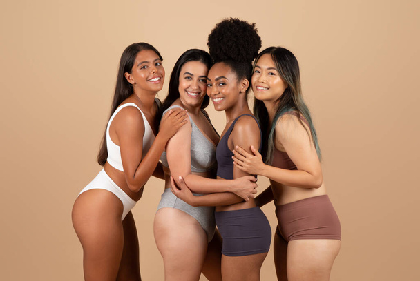 Vier vrienden van verschillende etniciteiten die vol vertrouwen poseren in ondergoed, met een tapijt van diverse schoonheid en kameraadschap tegen een beige studio achtergrond - Foto, afbeelding