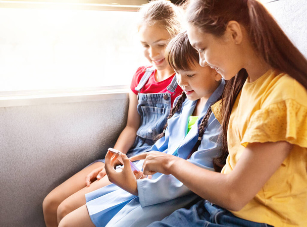 Grupo de niñas que usan teléfonos inteligentes juntos durante el viaje en autobús escolar, lindos niños femeninos que participan con el teléfono móvil, jugando juegos en línea o viendo fotos en el teléfono celular, espacio para copiar - Foto, imagen