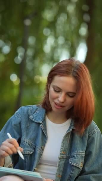 Eine schicke, junge Frau, die im Park mit einem Tablet arbeitet. Hochwertiges 4k Filmmaterial - Filmmaterial, Video