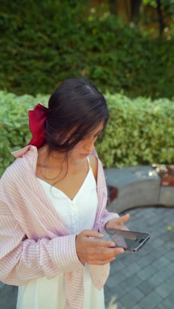 Eine kultivierte, junge Dame hält an einem sonnigen Tag ein Telefon in der Hand. Hochwertiges 4k Filmmaterial - Filmmaterial, Video