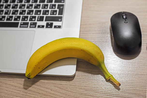 banaan op tafel naast de computer met een computermuis. tussendoortje - Foto, afbeelding