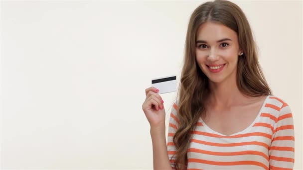 Viehättävä nuori tyttö näyttää peukalot pystyssä luottokortilla. Lähikuva muotokuva nuori hymyilevä nainen, jolla on luottokortti ja peukalo ylös merkki, eristetty valkoisella taustalla
. - Materiaali, video