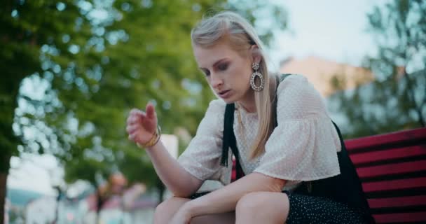 Depresyjna blondynka z głową w dłoni siedzi na ławce w ogrodzie podczas weekendu - Materiał filmowy, wideo