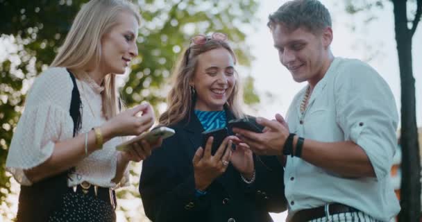 Χαμογελώντας νεαρές γυναίκες και άνδρες φίλους που χρησιμοποιούν κινητά τηλέφωνα, ενώ περνούν ελεύθερο χρόνο στον κήπο - Πλάνα, βίντεο