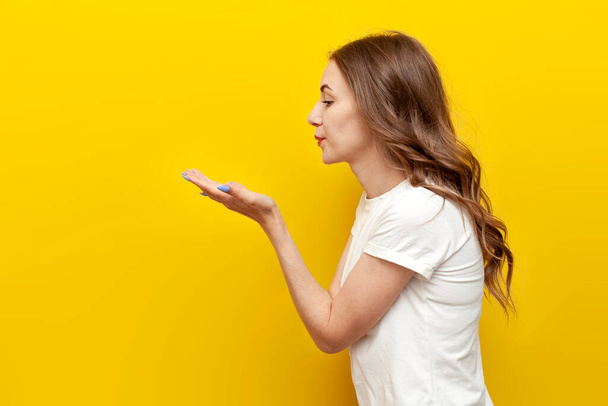 young cute girl sends air kiss to the side on yellow isolated background, woman flirts and shows gesture of romance and love - Photo, Image