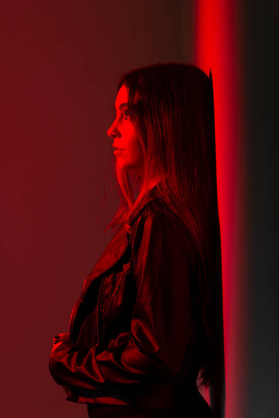 Schöne kaukasische Frau, die in schwarzen Kleidern vor einer knallroten Wand steht. Studioporträt - Foto, Bild