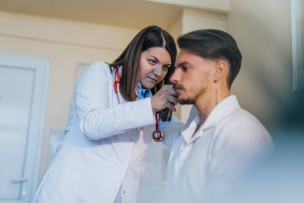 An experienced healthcare professional providing comprehensive medical care, checking blood pressure, blood sugar levels, and conducting a hearing exam in a well-equipped examination room. - Photo, Image
