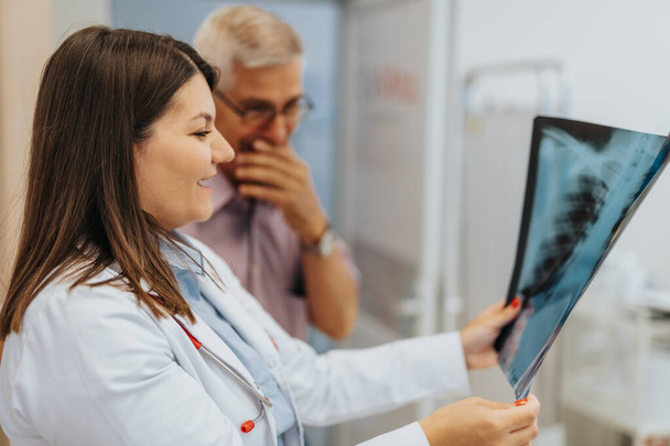 Um médico experiente analisando filmes de raios X, verificando pulmões, dando diagnóstico a um paciente em seu consultório. - Foto, Imagem