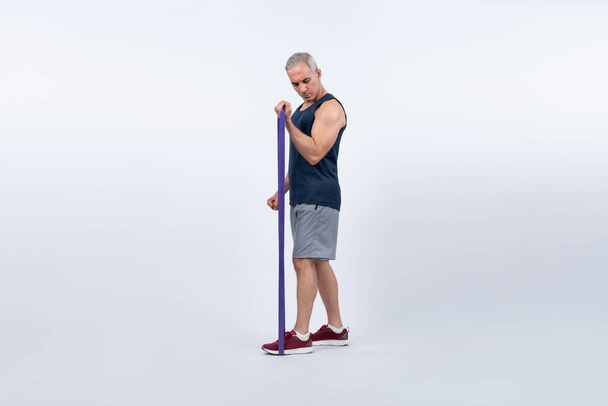 Teljes testhosszú lövés atlétikai és sportos idősebb férfi fitness rezisztencia sáv elszigetelt háttérrel. Egészséges aktív fizikum és testápoló életmód nyugdíjazás után. Kömény - Fotó, kép