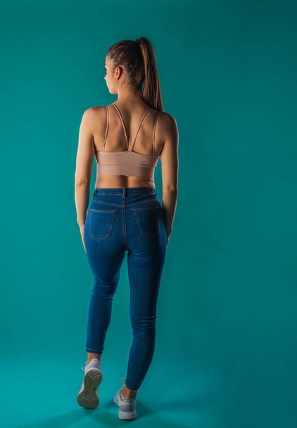 Selbstbewusstes weibliches Fitnessmodel posiert für Studioaufnahmen mit türkisfarbenem Hintergrund - Foto, Bild