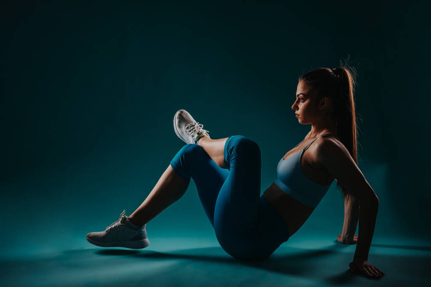 Uma jovem confiante em um estúdio escuro, mostrando sua poderosa transformação de fitness. - Foto, Imagem