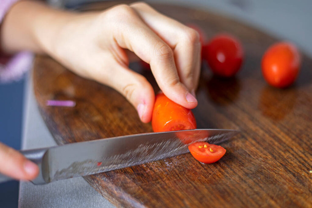 ręka dziecka tnie pomidora wiśniowego na plasterki na desce do krojenia - Zdjęcie, obraz