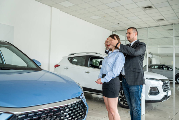 an extremely happy woman is happy when her husband bought a car at a car dealership. happy couple in salon. car purchase - Zdjęcie, obraz